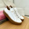 Eleganckie białe sportowe buty Ulmani z beżowym akcentem na pięcie i złotymi oczkami na sznurówki, umieszczone na drewnianym blacie.