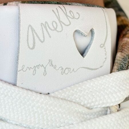 Zbliżenie na język buta – logo Anekke z wyciętym sercem i haftem „enjoy the now” – ażurowe sneakersy